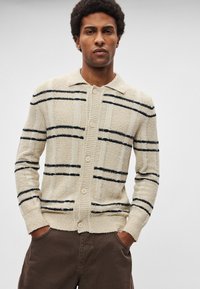 Bēša kardigāns ar tumši ziliem svītrām, faktūrēts audums, apkaklīte, piecas pogas un ribota aproce. Viegls dizains ar brīvu piegriezumu.