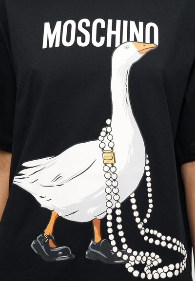Μαύρο μπλουζάκι με το κείμενο "MOSCHINO". Διαθέτει γραφικό λευκής χήνας που φοράει μαύρα παπούτσια και κρατάει περιδέραια από πέρλες.