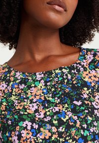 Close-up of a woman’s neck and lower face wearing a black floral top with multicolored small flowers in green, blue, orange, and purple.