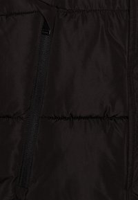 Svart puffjacka i tyg med en slät textur, med en framträdande dragkedja och kviltade sömmar. Inga mönster eller ytterligare detaljer synliga.
