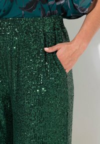 Groene paillettenbroek met een textuur ontwerp, een ontspannen pasvorm, een elastische tailleband en zijzakken. De pailletten weerkaatsen het licht en zorgen voor glans.