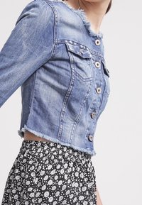 Jeansowa krótka kurtka z postrzępionym kołnierzem, czterema guzikami i dwiema kieszeniami na piersi. Połączona z czarną spódnicą w kwiatowy wzór.