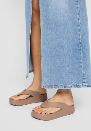 Des sandales à doigts brunes avec une semelle épaisse et une large bride, assorties d'une jupe en denim bleu clair avec une fente sur le côté et un ourlet effiloché.