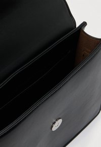 Mala de mão em pele preta com textura lisa, equipada com um único fecho de mola prateado e interior forrado a castanho com vários compartimentos.