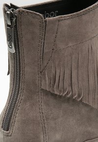 Botte de cheville en suédine grise avec une fermeture éclair sur le côté et un détail à franges le long du bord supérieur. Texture lisse avec un design à bout arrondi.