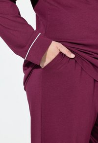 Completo da loungewear color bordeaux composto da un top a maniche lunghe e pantaloni. Il top presenta piping bianchi a contrasto, mentre i pantaloni sono dotati di tasche laterali.
