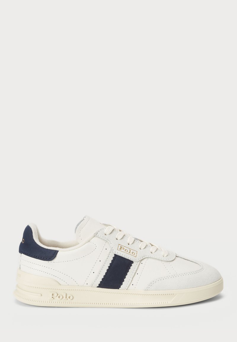 White sneaker with navy suede accents, lace-up design, textured rubber sole, and embossed logo. Features a smooth leather upper and contrasting stripe.