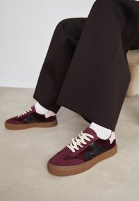 Burgundy mockaskor med svarta detajer, krämfärgade snören och en gummisula. Bred passform med kontrasterande rosa häl detaljer.