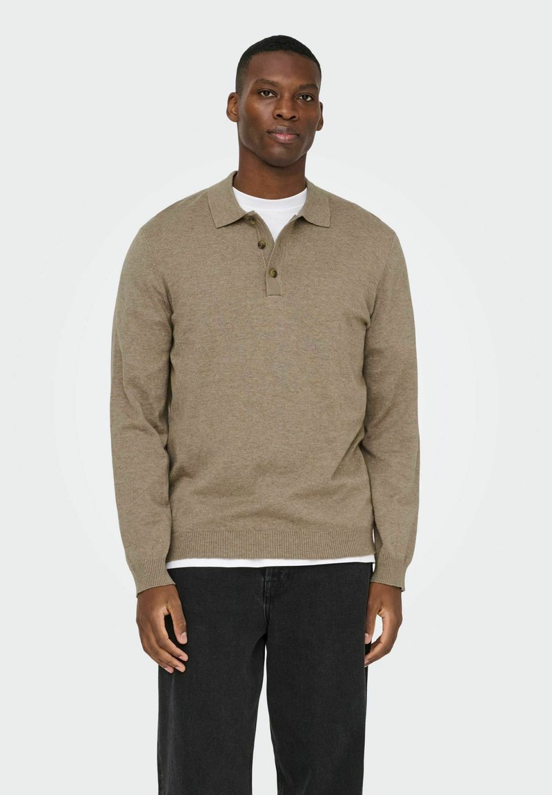 Jersey tejido de color marrón claro con cuello con solapa, tres botones, mangas largas y dobladillo acanalado, llevado sobre una camisa blanca.