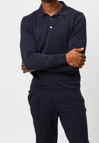 Marineblaues Langarm-Polohemd mit Kragen, ausgestattet mit einer Knopfleiste mit drei Knöpfen, gerippten Bündchen und Saum, hergestellt aus einem weichen, strukturierten Stoff.