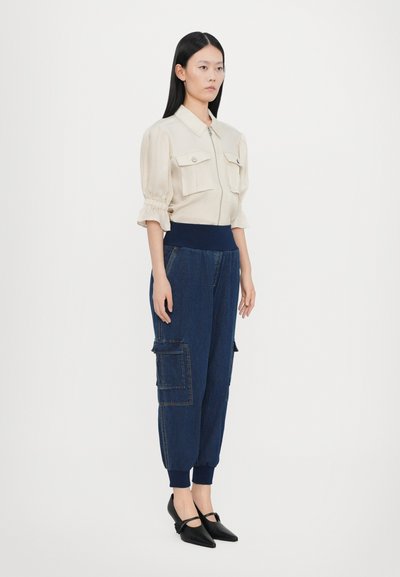 Beige blouse with puff sleeves and two chest pockets, paired with dark blue tapered cargo pants featuring side pockets. Black pointed flats.