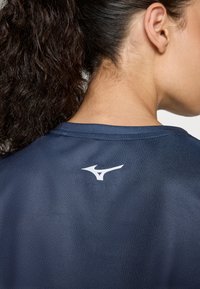 Tumed spordisärk sujuva tekstuuriga, millel on valge logo ülaseljal ja klassikaline ümar kaelus.