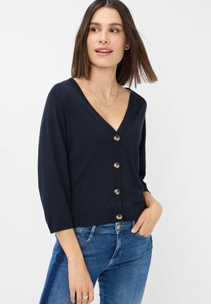 Cardigan col en V marine en tissu doux, avec six boutons ronds à l'avant et des manches trois-quarts. Assorti avec un jean bleu.