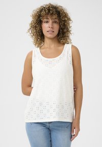 Top senza maniche bianco con ritagli decorativi, scollatura rotonda e vestibilità ampia, abbinato a jeans azzurri chiari.