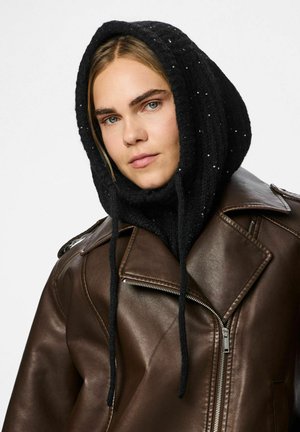 Sort strikket hætte med pailletdetaljer, parret med en brun læderjakke med en klapkrave og lynlås foran.
