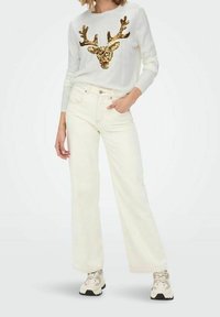 Witte trui met een glinsterend rendierontwerp, gecombineerd met off-white wijde jeans en beige sneakers. Stoere stof met geribbelde manchetten.