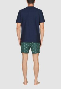 T-shirt a maniche corte blu della marina abbinato a pantaloni da mare verdi con pattern di pesci bianchi. Tessuto liscio visibile e vestibilità comoda.