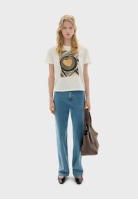 White short-sleeve t-shirt featuring a heart-shaped design on a plate, paired with light blue straight-leg jeans and a gray tote bag.