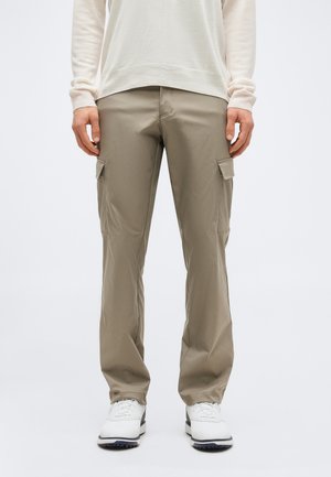 Μπεζ παντελόνι cargo με ευθεία γραμμή και πλαϊνές τσέπες με καπάκι, συνδυασμένο με λευκά αθλητικά παπούτσια και ανοιχτό κρεμ μακρυμάνικο τοπ.