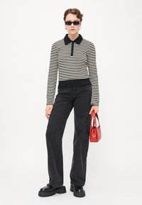 Polo a maniche lunghe a righe in nero e crema, con colletto e chiusura a bottoni. Abbinato a jeans neri a vita alta con gamba larga e una borsa rossa.