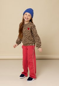 Sweatshirt met luipaardprint en rode hartdetails, gecombineerd met roze joggingbroek met witte zijkanten en blauwe sneakers.