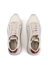 Zapatillas deportivas de color crema con acentos beige, cuero texturizado, detalles dorados y un talón de purpurina roja. Diseño con cordones y lengüeta acolchada.