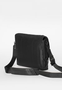 Zwarte boodschappentas met een glad leren buitenkant, verstelbare schouderriem en een zijvak met rits. Kenmerkt zich door een eenvoudig, modern ontwerp.