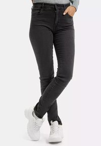 Ciemnoszare wąskie jeansy z wysokim stanem, z przednimi kieszeniami i subtelnymi detalami w przeszyciach, w zestawieniu z białymi sneakerami.