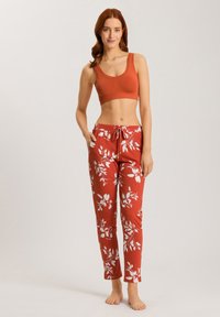 Rustkleurige crop top gecombineerd met witte loungebroeken met bloemenpatroon en trekkoorden. Zachte stof, getailleerde pasvorm en relaxte silhouet.