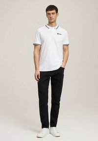 Biała koszulka polo z czarnymi akcentami i logo, w połączeniu z czarnymi spodniami i białymi trampkami. Prosty, dopasowany krój z krótkimi rękawami.