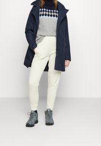 Marinblå vattentät jacka, grå tröja med blå geometriskt mönster, krämfärgade joggers och blå vandringsskor med texturerade snören och gummisålar.