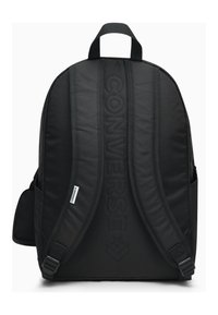 Mochila negra con correas de hombro acolchadas y detalle del logo en relieve en el frente. Cuenta con bolsillos laterales, una tela suave y un asa superior resistente.