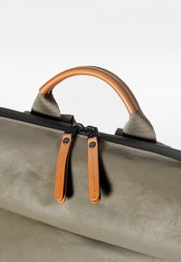 Borsa in tela verde con manico in pelle marrone, chiusura con zip e due tirazip in pelle marrone. Presenta un materiale testurizzato e un design minimalista.