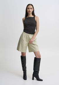 Must mustriba tank top, heledad rohelised plisseeritud lühikesed püksid ja kõrged mustad nahast kontsakingad. Lihtne disain sujuvate tekstuuride ja neutraalsete värvidega.