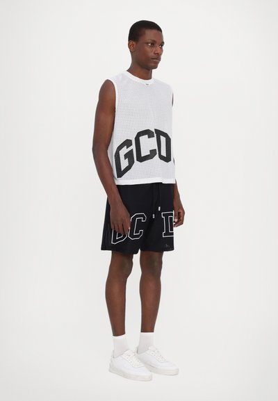 Top senza maniche bianco in rete con lettering nero "GCD", abbinato a pantaloni corti neri con accenti bianchi "DC" e scarpe da ginnastica bianche.