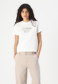 Hvit bomulls t-skjorte med "Carhartt WIP" i glitrende sølvbokstaver. Kombinert med beige, høytlivsbukser, og stoffet ser mykt ut.