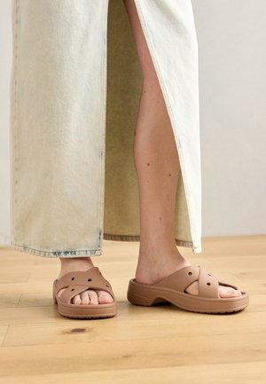 Barna gumiszandál széles pántokkal és szellőző lyukakkal, világoskék farmerszoknyával viselve, amelynek oldalsó része hasított.