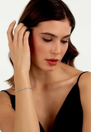 Bracciale argento con gemme trasparenti in una linea continua, con un piccolo pezzo di accentuazione gialla. Indossato su un braccio di tonalità della pelle chiara.