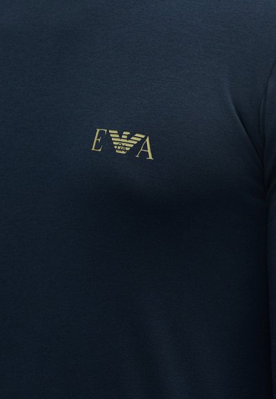 Σκούρο μπλε ύφασμα με μικρό χρυσό λογότυπο Emporio Armani που παρουσιάζει στυλιζαρισμένο αετό και τα γράμματα E και A στην περιοχή του στήθους.