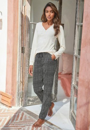 Long-sleeve cream top with a V-neck and buttons, paired with black check-patterned pants featuring an elastic waistband and side pockets.