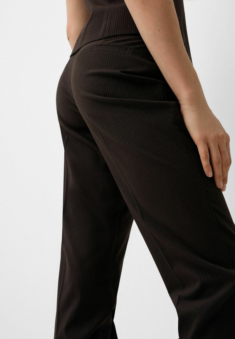 Pantaloni marrone a righe con un design sartoriale, caratterizzati da una texture liscia e una silhouette aderente. Tasca posteriore visibile sul lato destro.