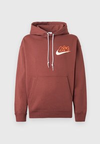 Sweat à capuche couleur rouille avec cordons blancs et poche avant, avec un petit logo orange et blanc de style Nike sur la poitrine gauche.