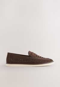 Mocassin en cuir marron avec des détails tissés sur les côtés et le dessus, semelle blanche en caoutchouc et style slip-on.