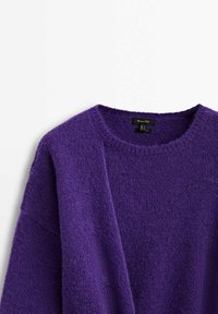 Pull col rond violet avec une texture douce et duveteuse en tricot et une étiquette de marque visible à l'intérieur du col.