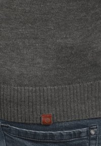 Grijze gebreide trui met geribbelde zoom. Heeft een klein bruin label aan de onderkant. Combinatie met donkerblauwe denim broeken.