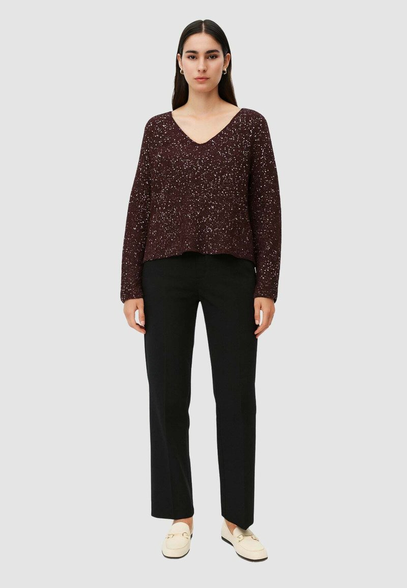 Pullover in magenta con scollo a V, maniche lunghe e vestibilità rilassata, abbinato a pantaloni neri a gamba dritta e scarpe bianche slip-on.