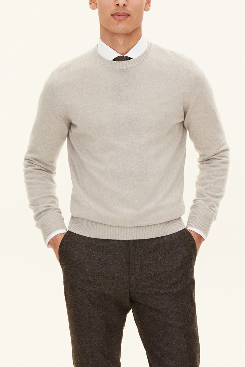 Pull en tricot gris clair à col rond, avec des poignets et un ourlet côtelés, associé à un pantalon texturé foncé.