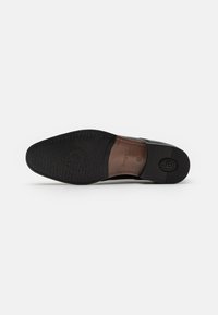 Semelle d'une chaussure habillée pour homme en cuir noir avec avant et talon en caoutchouc noir texturé, partie médiane en cuir marron, et "bugatti" embossé sur la semelle.