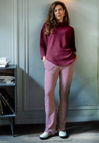 Bordeauxkleurige wollen trui met een losse pasvorm, gecombineerd met gestreepte, rechte broek in roze en witte ruiten, afgewerkt met groene schoenen.