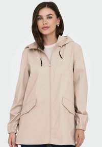 Chaqueta beige con capucha, puños elásticos, cierre de cremallera y dos bolsillos delanteros. Fabricada con material suave y resistente al agua.